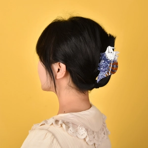 Macro side view of a blue and white acetate dinosaur hair claw clip on short black hair