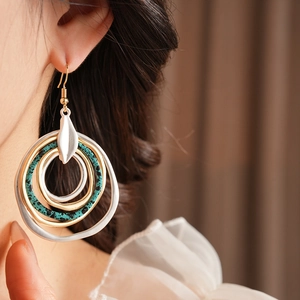 Close-up of layered circular drop earrings with silver, gold and teal spotted hoops on a model