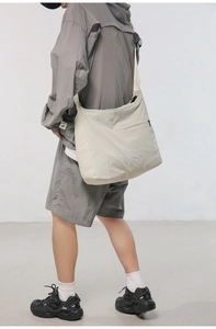 Side view of a cream white nylon crossbody bag worn by a model for size and drape