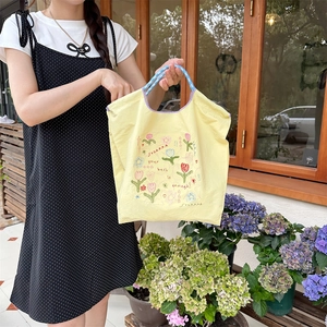 Detail der Blumenstickerei und des Textes auf gelber Canvas-Tasche im Freien