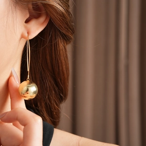 Gros plan de boucles d'oreilles boules dorées texturées portées sous une lumière douce