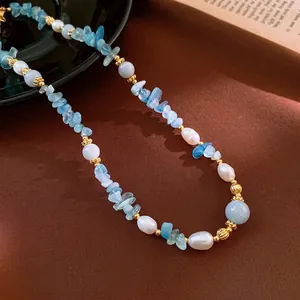 Blue aquamarine stone and white pearl necklace with gold metal beads on brown fabric