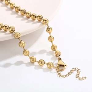 Golden stainless steel heart bead chain necklace set shown on a white ceramic plate