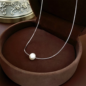 Gros plan d'un collier argenté avec une perle blanche dans un écrin à bijoux marron chic