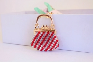 Macro shot of gold handbag keychain with red and white rhinestone stripes on white box