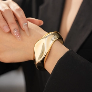 Polished gold fluid wave wide open cuff bracelet worn on a model with black suit