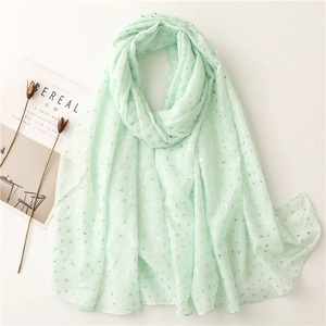 Detail of mint green scarf with gold floral patterns on a minimal white background