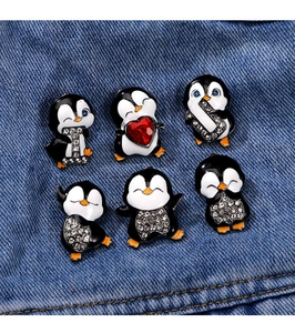 Detail view of six cute penguin enamel pins with rhinestones on blue denim fabric