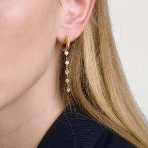 Détail de boucles d'oreilles à pompons dorés avec cinq zircons portées par un modèle