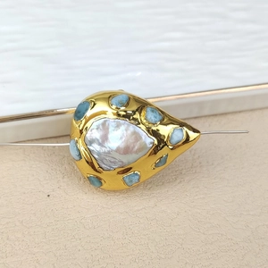 Close-up of teardrop pearl pendant with blue turquoise beads on golden tray