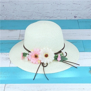 Detail of white woven straw hat featuring decorative brown cord and daisy flower accents