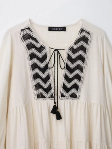 Detail of V-neckline with tassel ties and black-white wave embroidery on cream dress