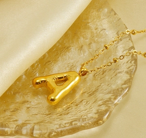 Macro shot of gold-plated puffy letter A pendant with beaded cross chain on satin