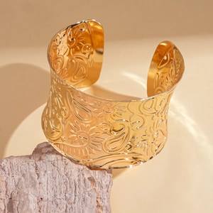 Close-up of wide golden open cuff with embossed floral and paisley patterns