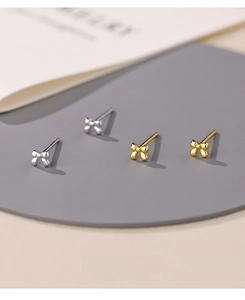 Close-up of gold and silver S999 sterling silver mini bow stud earrings on display