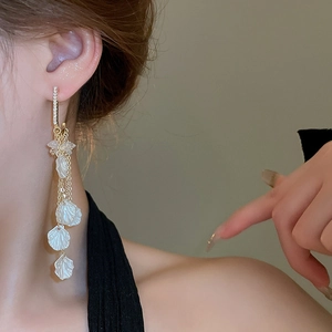 Détails de boucles d'oreilles pétales de nacre avec diamants et longs glands sur le mannequin