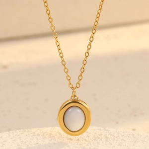 Golden oval stainless steel necklace with white shell inlay on a minimalist stone background