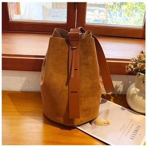 Detailed close-up of tan suede bucket bag with wide strap on a rustic wooden table