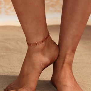 Close-up of a layered gold stainless steel anklet with small beads on a beach
