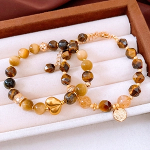 Dettaglio di bracciali in perle di occhio di tigre placcati oro 18k con ciondoli a cuore