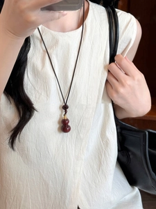 Close-up of red wooden gourd pendant on black cord worn with beige linen clothing