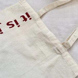 Gros plan du sac fourre-tout en toile beige avec poignées renforcées et texte rouge