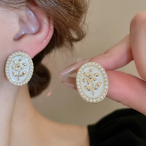 Macro detail of French vintage pearl flower earrings with gold plating and white enamel