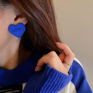 Detail of Klein blue heart stud earrings with LOVE relief pattern worn by model