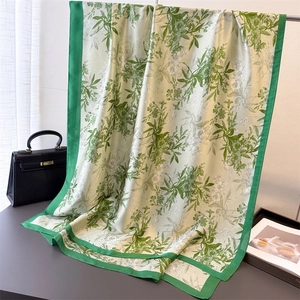 Detailed view of floral silk scarf with ivory base and green edges on a textured surface