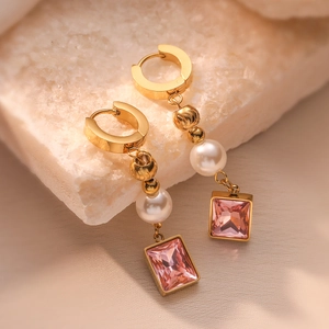 Elegant gold drop earrings with pink gemstone and white pearl on textured stone