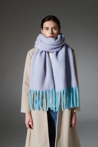 Close-up of lilac and blue knit scarf with thick tassels shown on a beige coat