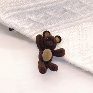 Gros plan sur la barrette ours marron foncé sur fond de tricot doux et page de livre