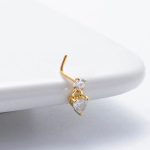 Macro detail of gold L-shaped nose stud with sparkling round and heart zircon pendants