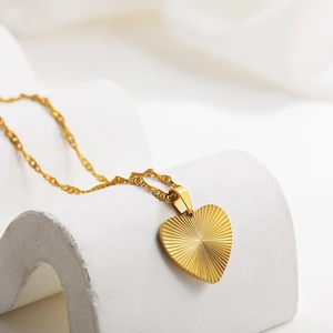 Close-up of 18k gold heart pendant with sunburst texture and twisted chain on stone stand