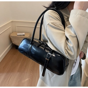 Close-up of a glossy black leather baguette bag worn by a model in a minimal setting