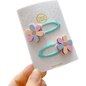 Pair of blue glitter hair clips with colorful felt flowers on a gold polka dot card