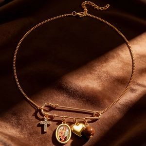 Detailed shot of golden safety pin necklace with religious medal and heart charm