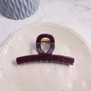 Detail of large dark purple hair claw clip with golden spring on ceramic tray