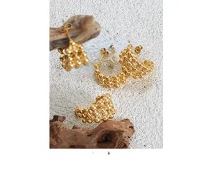 Detail of C-shaped gold beaded hoop earrings displayed on a natural wooden stand