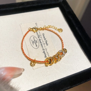 Détail d'un bracelet tressé rouge avec des breloques dorées et un fermoir mousqueton