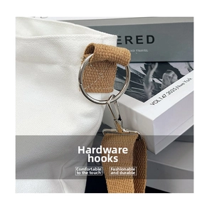 Detail of white canvas bag featuring sturdy brown woven strap and silver metal hook