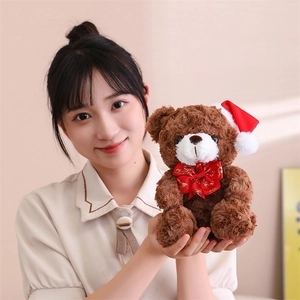 Close-up of soft brown plush teddy bear wearing a red Christmas hat and gold patterned bow