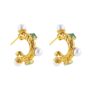 Detail of C-shape gold earrings with white pearls and square green emerald stones
