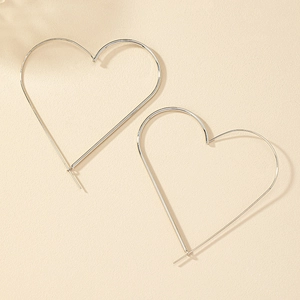 Close-up of oversized silver heart-shaped hoop earrings on a textured background