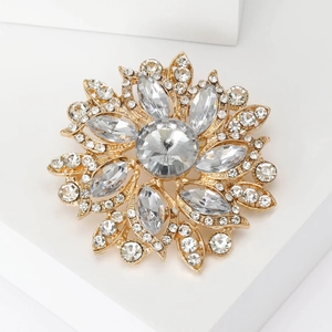 Macro shot of gold floral brooch featuring sparkling crystal rhinestones on a white pedestal