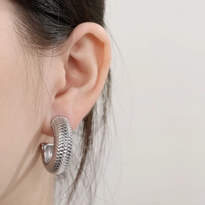 Close-up of silver C-shape hoop earring with snake skin texture on female model's ear