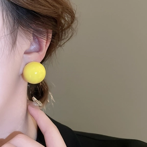 Close-up of a vibrant yellow spherical stud earring worn by a model for size and style