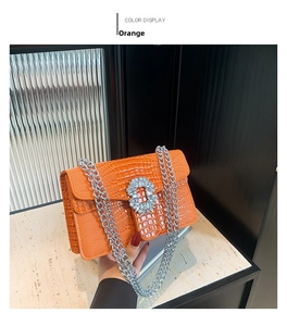 Close-up of orange crocodile pattern leather bag featuring a silver chain and rhinestone buckle