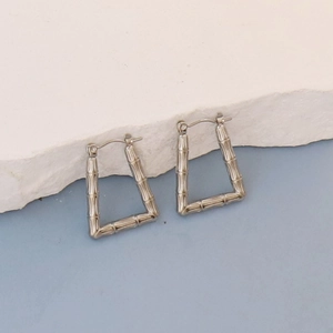 Detailed view of silver oval earrings with bamboo texture on a white stone background