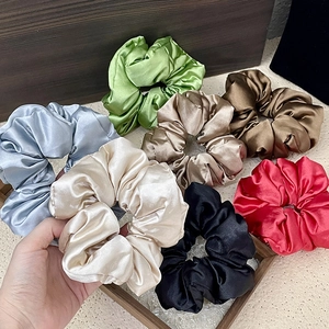 Set of seven satin silk scrunchies in diverse colors shown on a minimalist wood surface